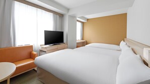 Habitación de hotel con una cama grande, un televisor en una mesita de noche de madera, un sofá y una pequeña mesa.