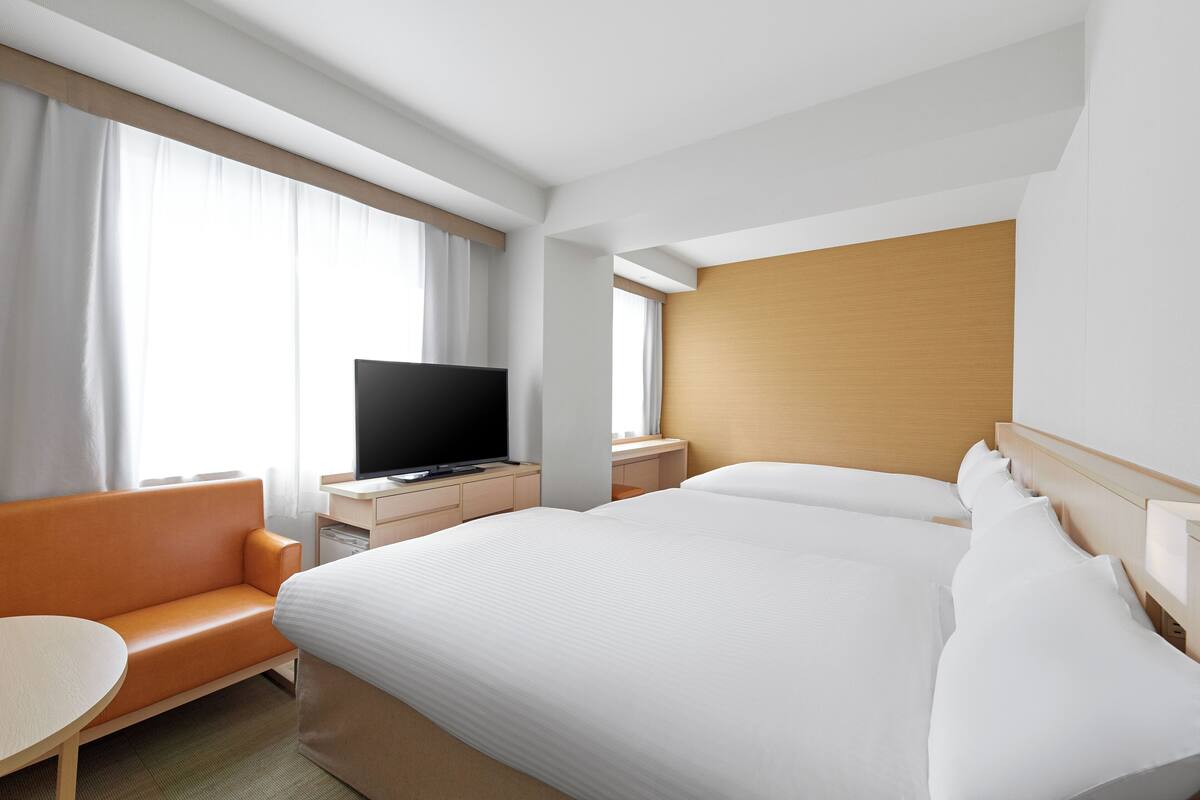 A hotel room with a large bed, a TV on a wooden nightstand, a sofa, and a small table.