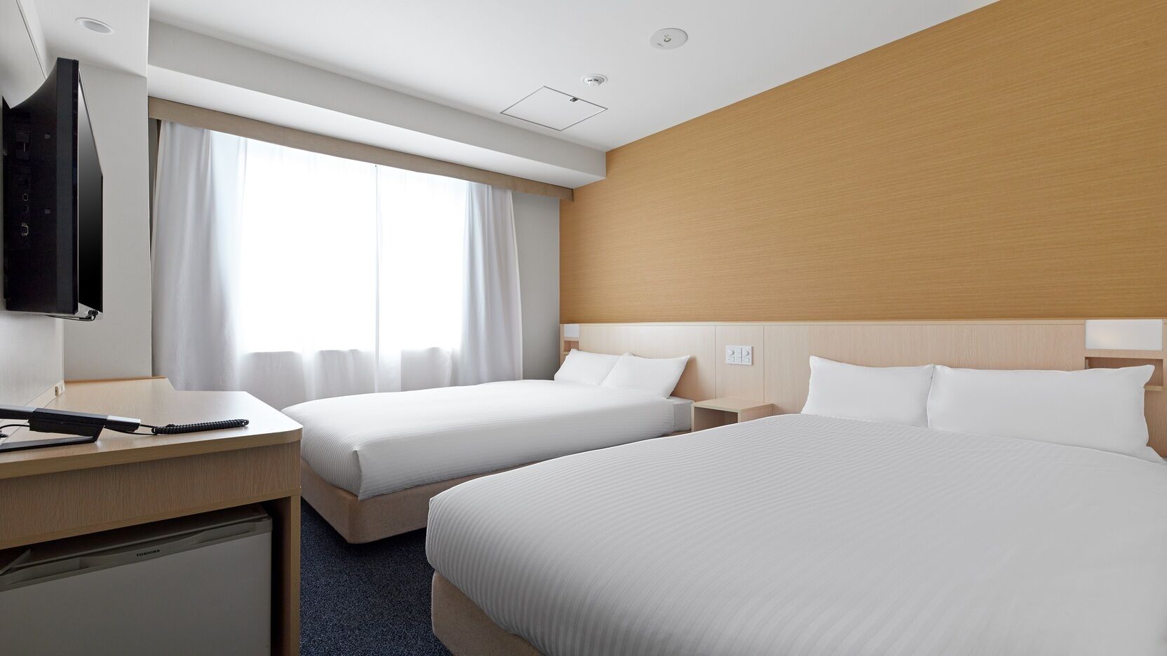 Habitación de hotel con dos camas, un escritorio, televisor y una ventana con cortinas.