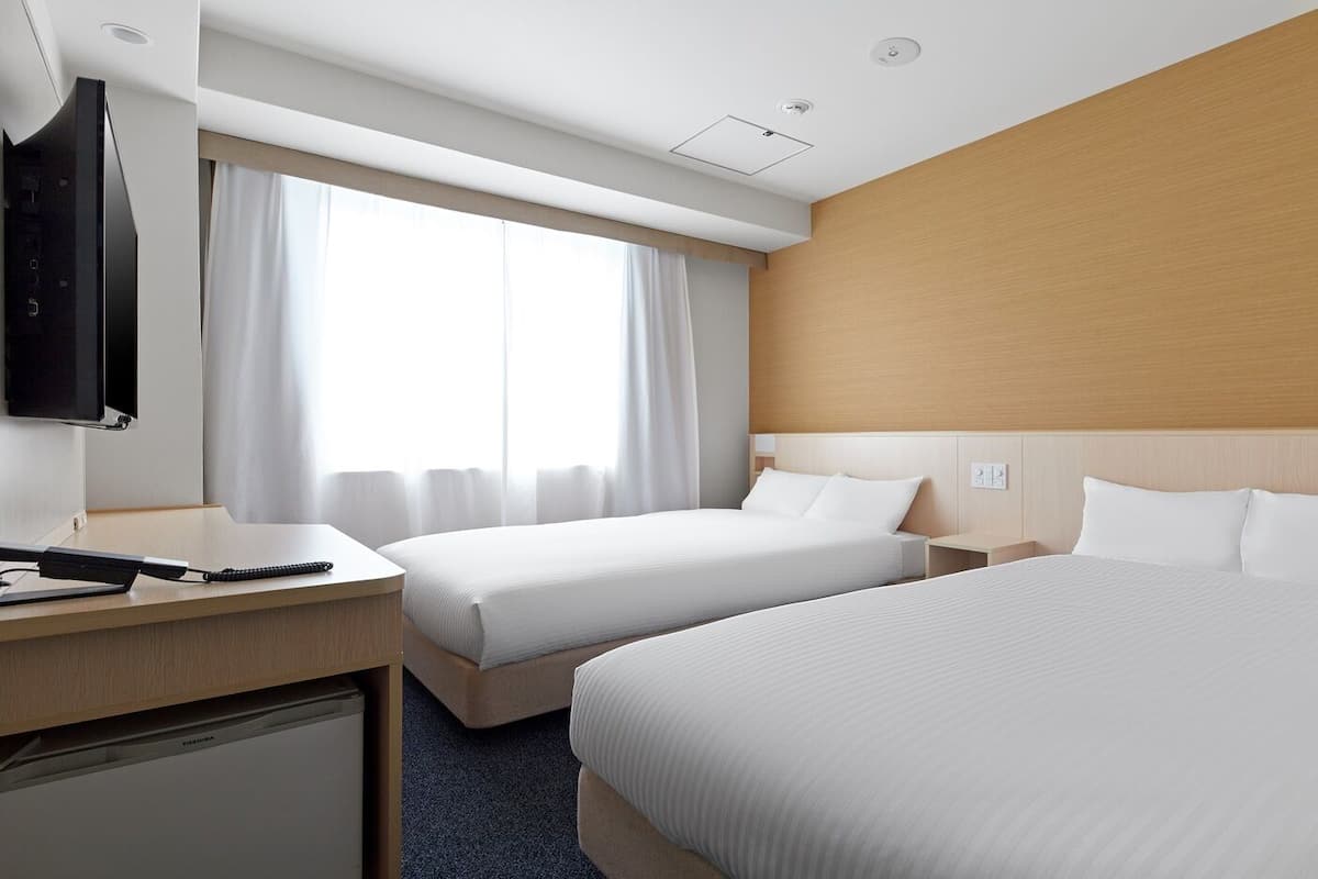 A hotel room with two beds, a desk, a television, and a window with curtains.