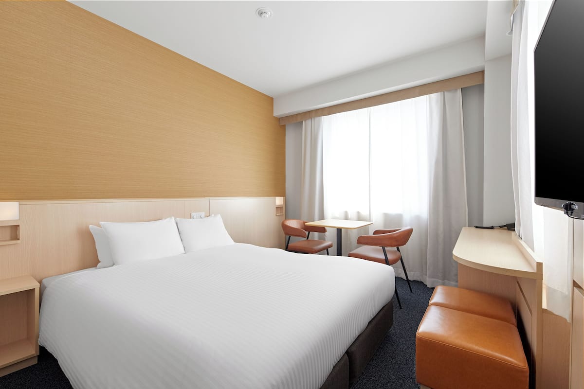 A hotel room with a large bed, a desk with a chair, a television, and a window with curtains.