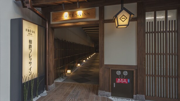 Una entrada tradicional japonesa con un portón de madera, un letrero que dice 'FRESAIN' y un farol.