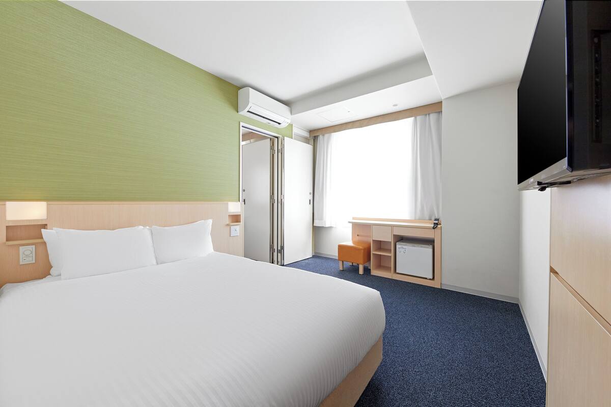 A hotel room with a large bed, a desk, a chair, a TV, and a window with curtains.