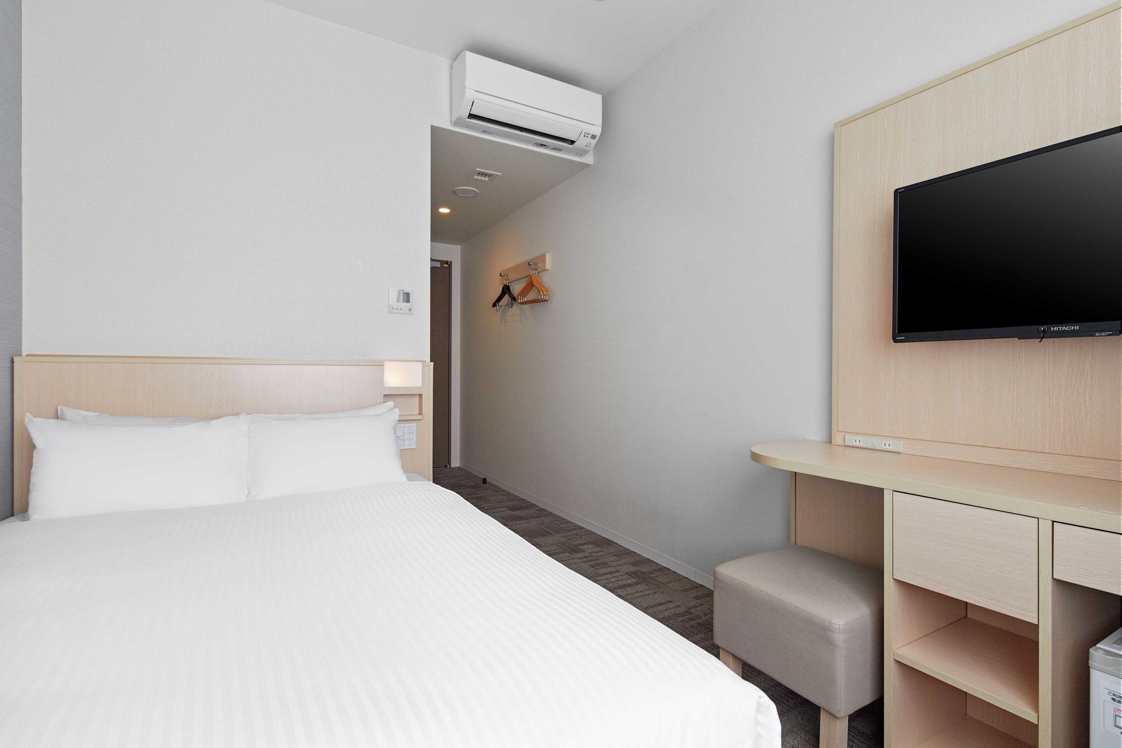A hotel room with a bed, a desk, a television, and an air conditioning unit.