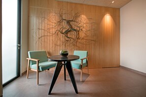 A room with two light green chairs, a round table with a black base, and a wall-mounted abstract art piece. - Tama Boutique Hotel (Bandung)