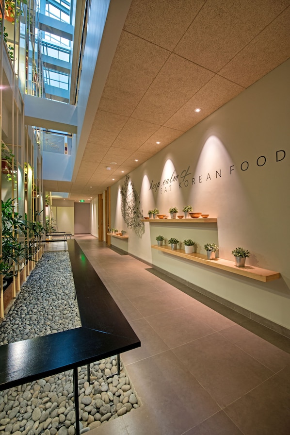 A modern interior with a long corridor, potted plants, and a wall with 'keep calm & eat Korean food' signage.