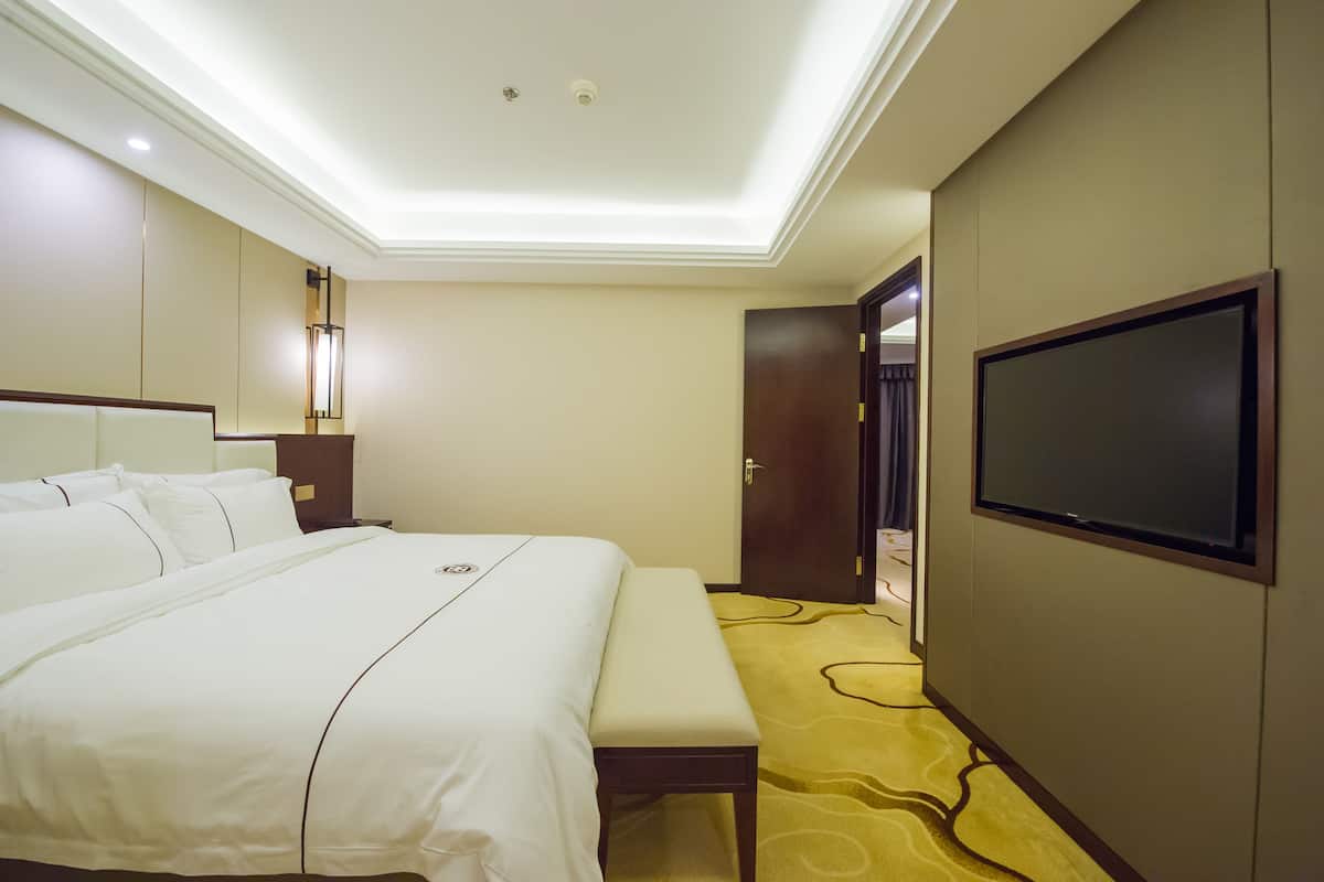 Une chambre d’hôtel avec un grand lit, un banc, un téléviseur à écran plat et une porte donnant sur une autre pièce.