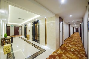 Un pasillo de hotel con piso de mármol, alfombra estampada y un ascensor moderno.