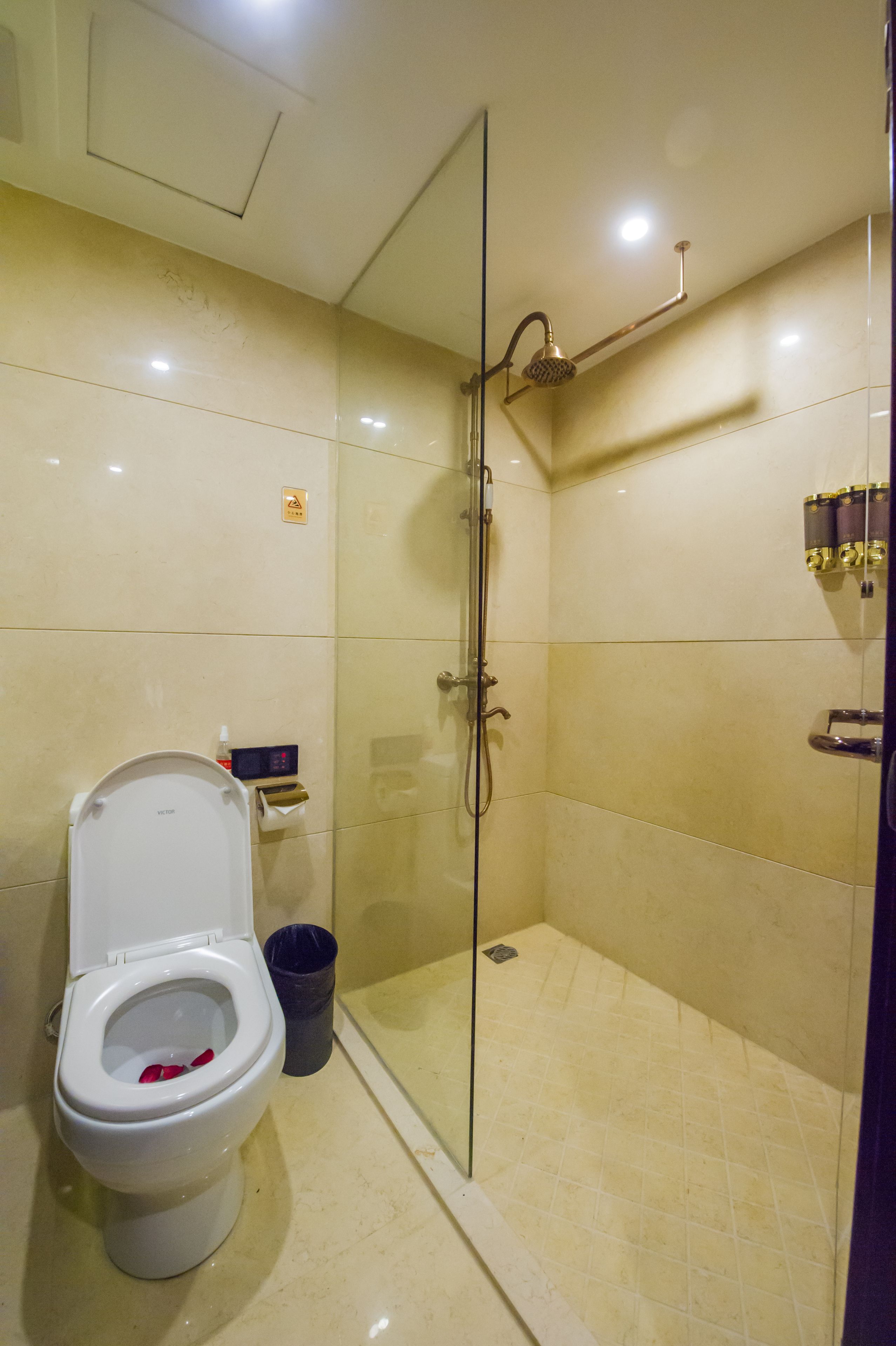 A bathroom with a toilet, a glass-enclosed shower, and a trash bin.