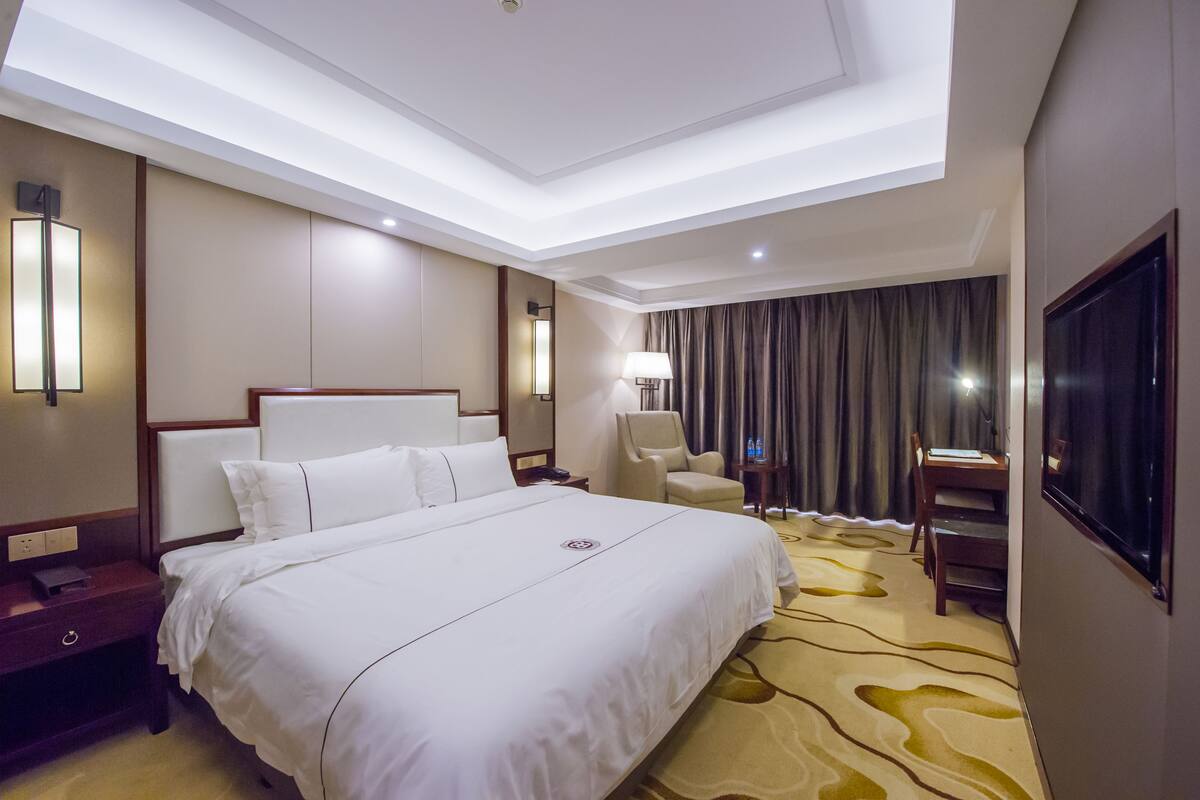 Une chambre d’hôtel avec un grand lit, un bureau, une chaise, une lampe et un téléviseur.