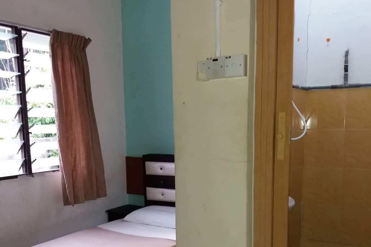 A room with a bed, a window with curtains, a wooden door, and a tiled shower area.