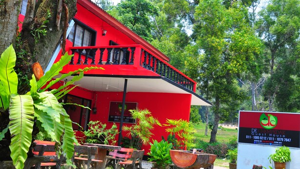 Un bâtiment rouge doté d’un balcon, entouré de verdure et agrémenté de plantes en pot.