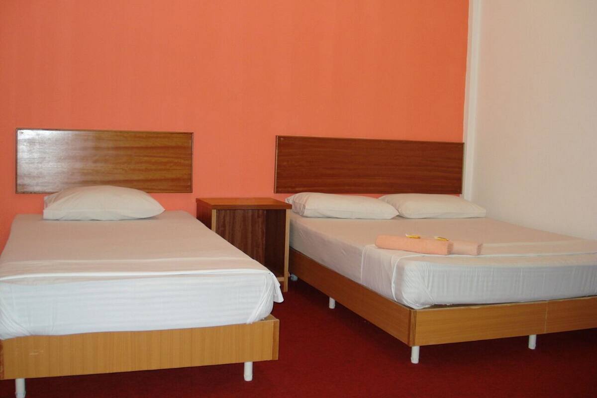 A room with two single beds, each with a wooden headboard and white bedding. There is a small wooden nightstand between the beds.