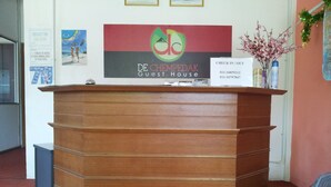 Un comptoir d’accueil en bois avec une enseigne indiquant « De ChempeDak Guest House » et une autre indiquant « Arrivée / Départ ».