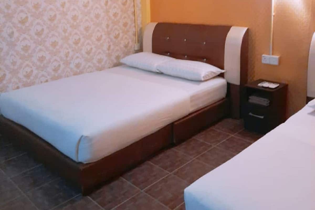 A hotel room with a single bed, a nightstand, a wall-mounted lamp, and a framed picture on the wall.