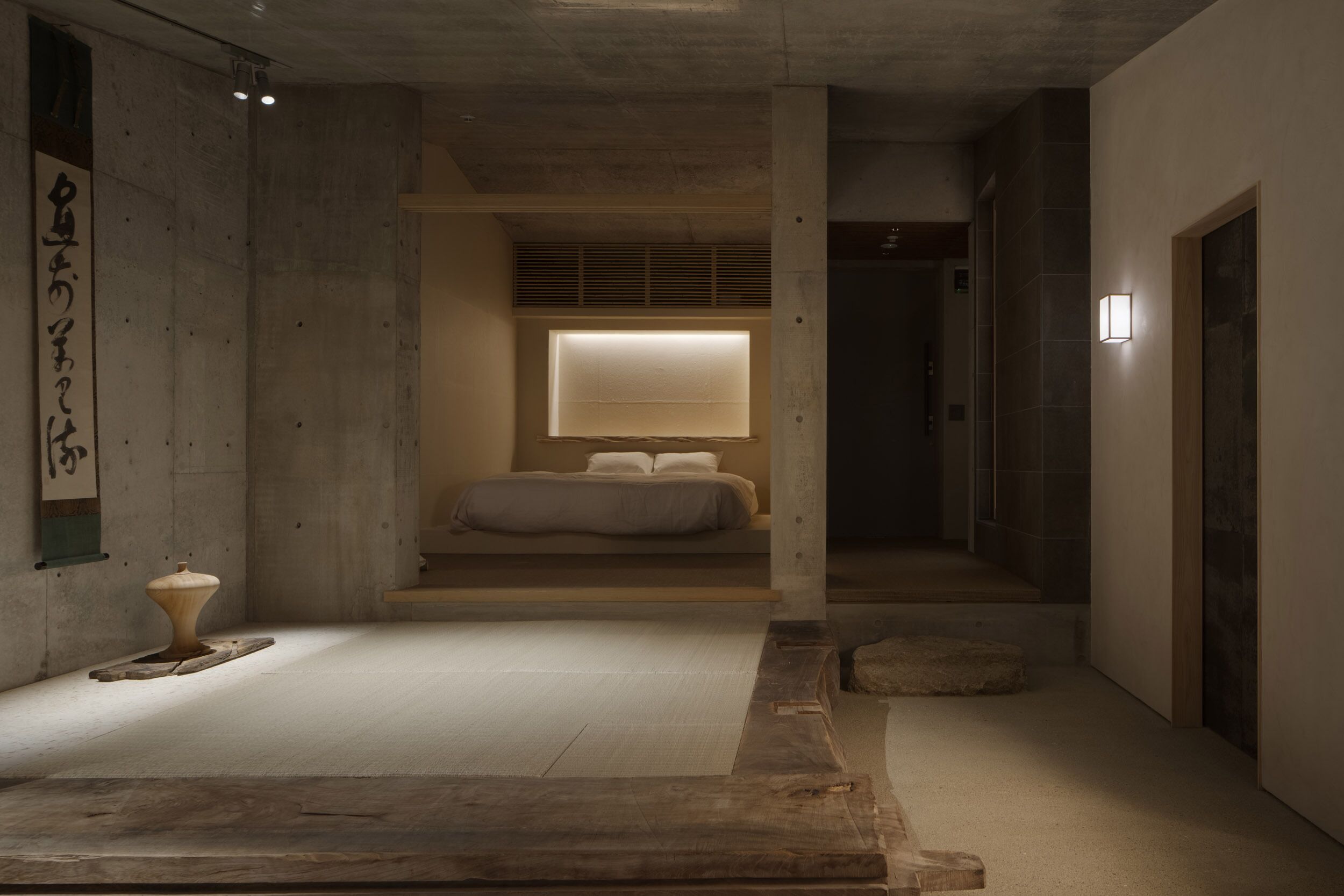 A minimalist room with a bed, a small table, and a wall-mounted light fixture.