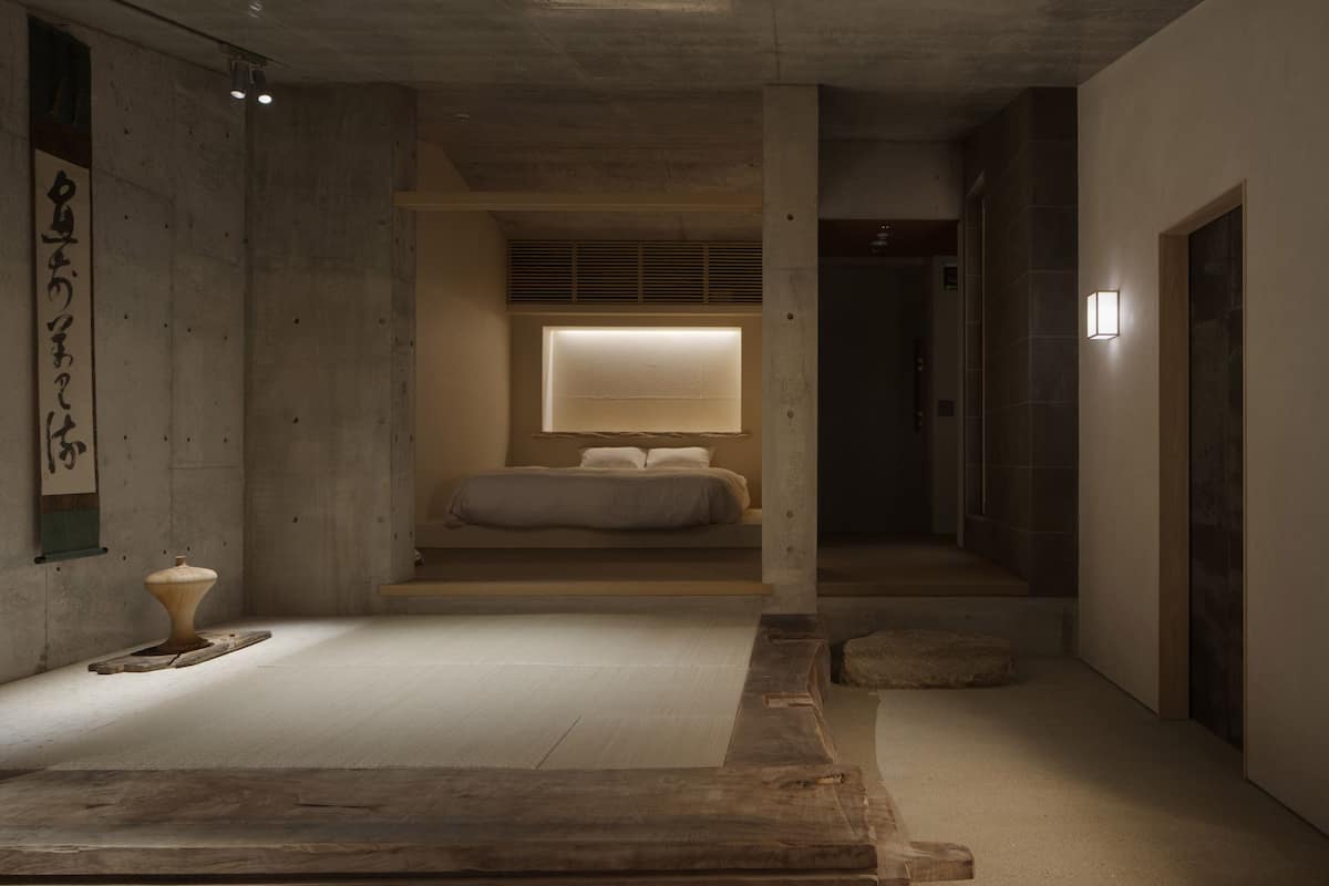A minimalist room with a bed, a small table, and a wall-mounted light fixture.