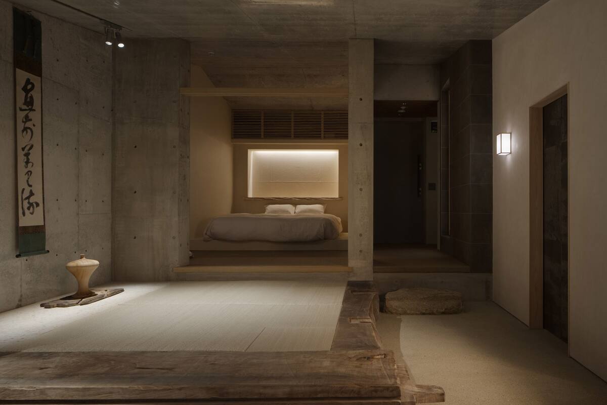 A minimalist room with a bed, a small table, and a wall-mounted light fixture.