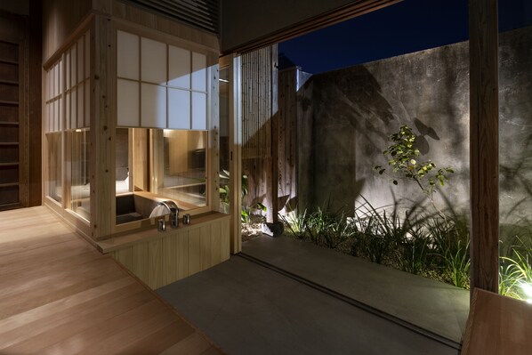 A modern bathroom with a wooden bathtub, a sink, and a glass enclosure.
