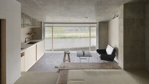 A modern kitchen with large windows, a dining area with a table and chairs, and a view of a body of water. - Kamohan (Kyoto)