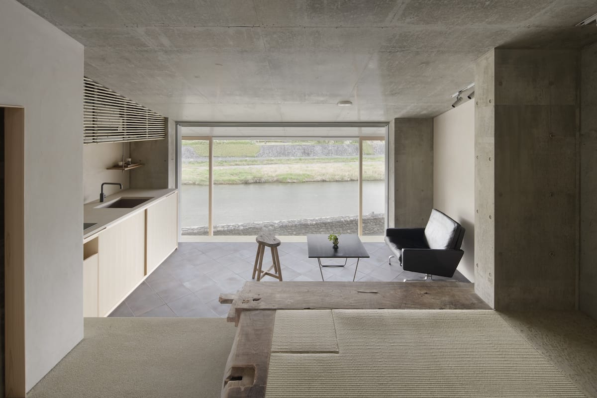 A modern kitchen with large windows, a dining area with a table and chairs, and a view of a body of water.