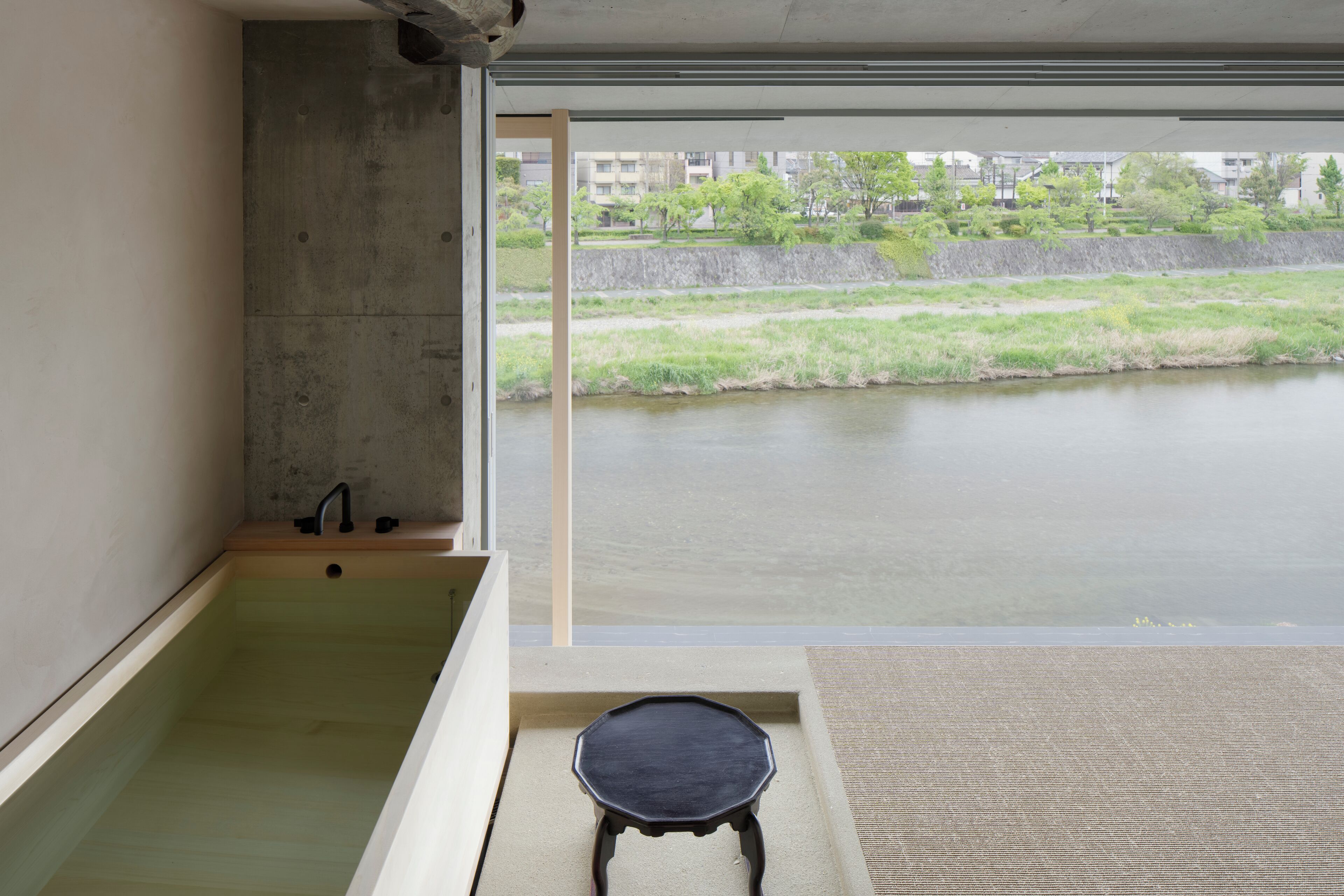 Un baño moderno con una bañera, un taburete pequeño y vistas a un río y edificios.