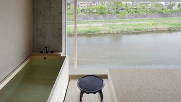 Un baño moderno con una bañera, un taburete pequeño y vistas a un río y edificios.
