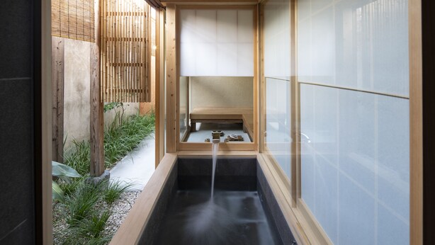 A traditional Japanese-style bath with a wooden frame, a black basin, and a small shelf with items. - Kamohan (Kyoto)