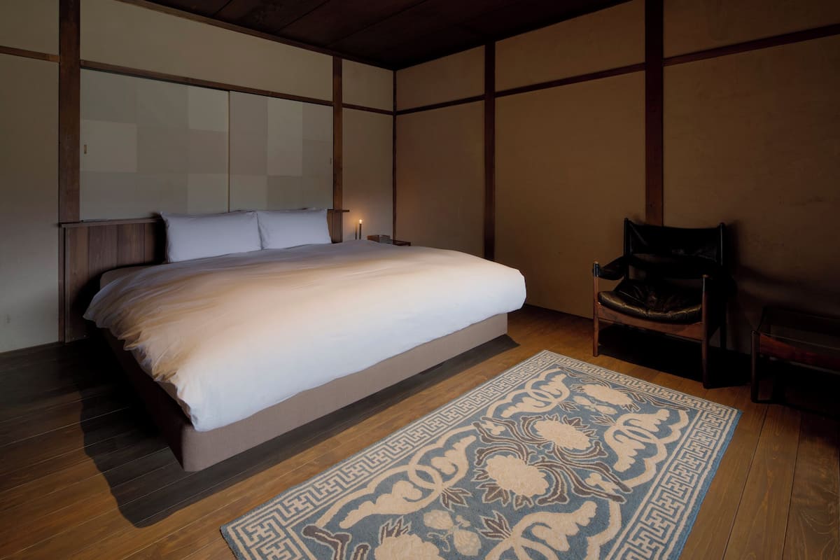 Un dormitorio con cama, una silla, un tapete y paneles de madera en las paredes.