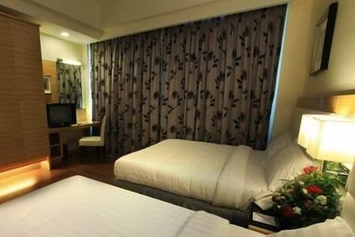 A hotel room with two beds, a desk, a television, and a curtain with a floral pattern.