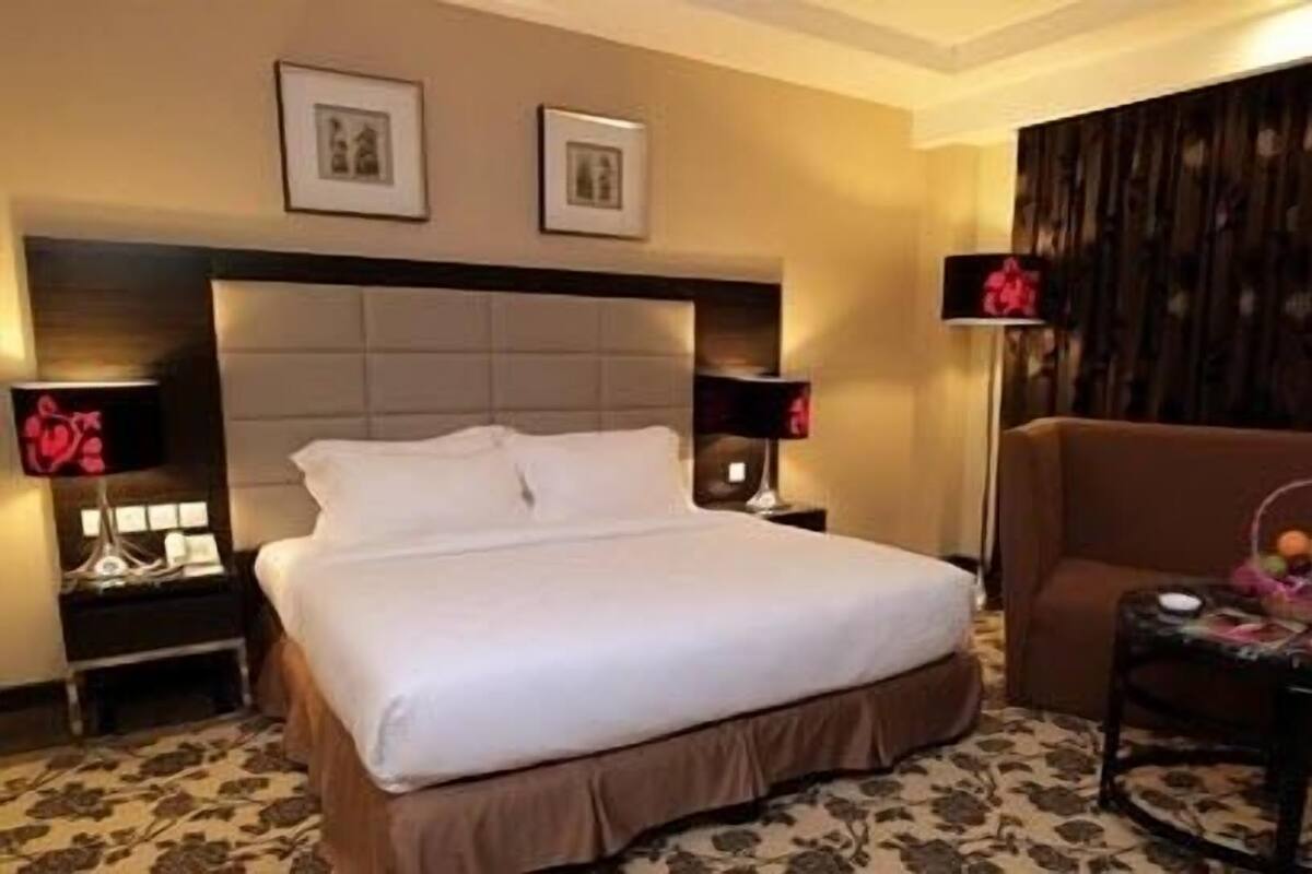 A hotel room with a large bed, two bedside tables with lamps, a brown armchair, and a small table with a basket.