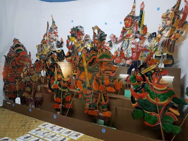 A display of traditional masks and figures in vibrant colors, arranged on a stand. - Crown Garden Hotel (Kota Bharu)