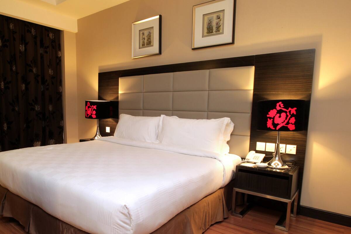 A hotel room with a large bed, two bedside tables, a headboard, and two framed pictures on the wall.