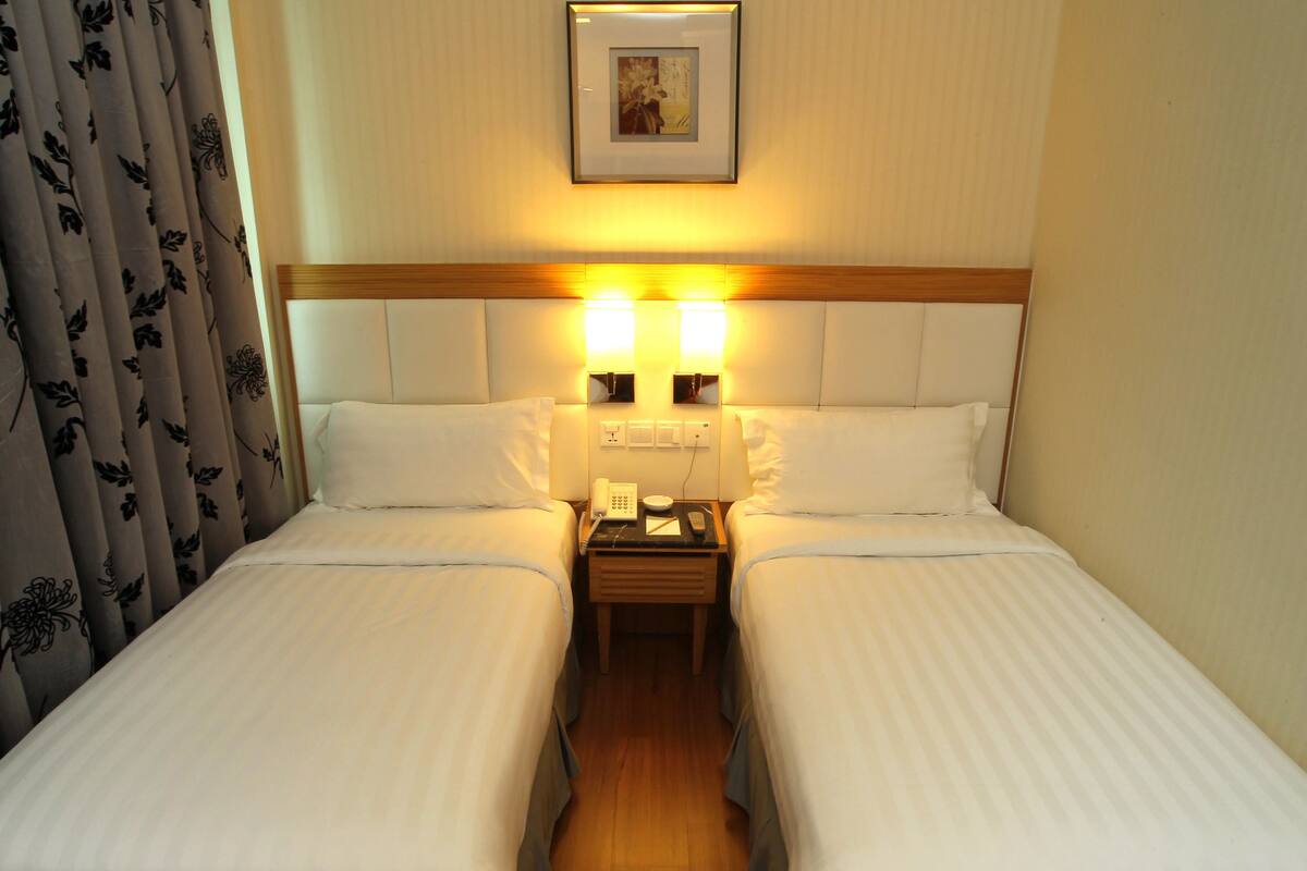 A hotel room with two single beds, a bedside table with a phone and a remote, and a framed picture on the wall.