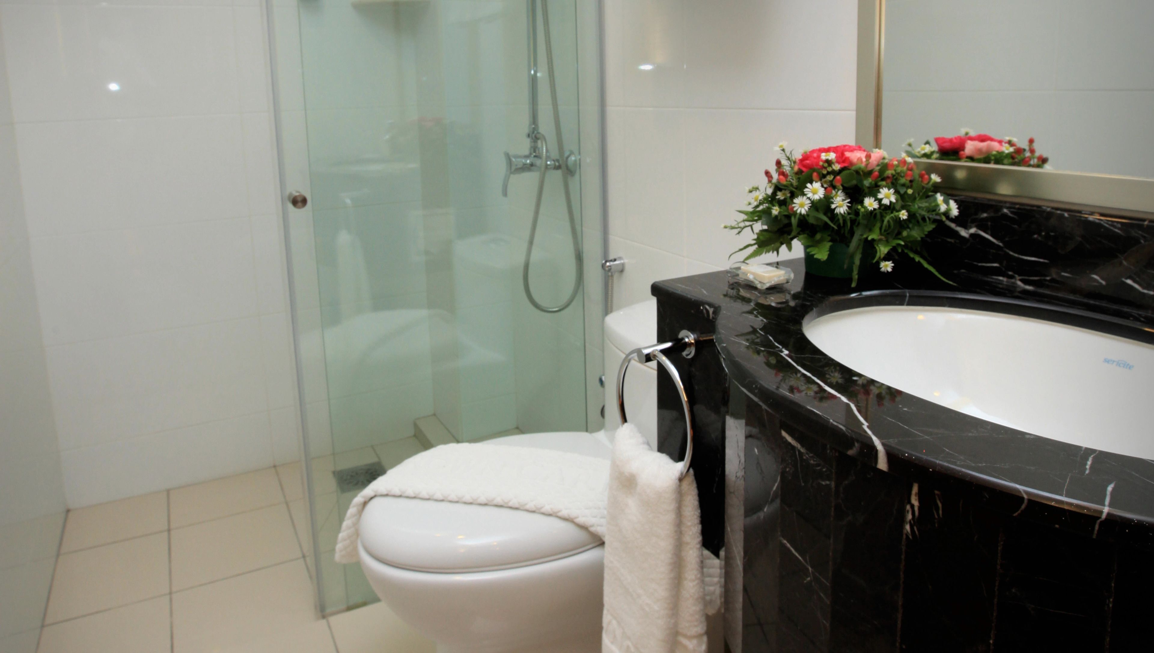 A bathroom with a glass-enclosed shower, a white toilet, a black marble sink, and a floral arrangement on the sink.