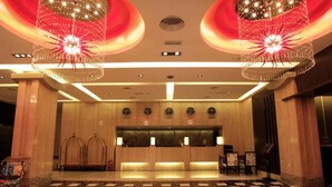 A hotel lobby with a reception desk, two large chandeliers, and a check-in counter.