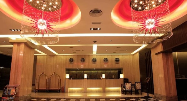 A hotel lobby with a reception desk, two large chandeliers, and a check-in counter.