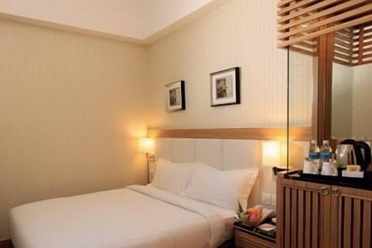 A hotel room with a bed, a nightstand, a mirror, and two framed pictures on the wall.