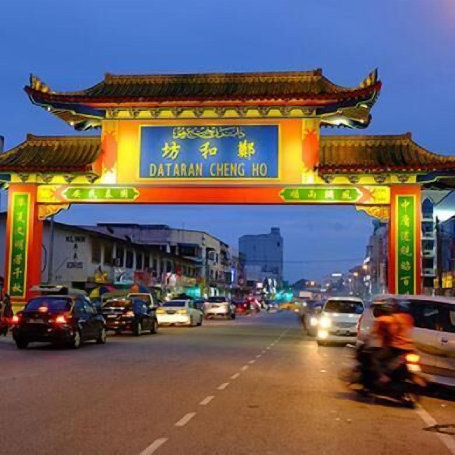 Escena callejera con un arco tradicional chino que dice "DATARAN CHENG HO" al anochecer.