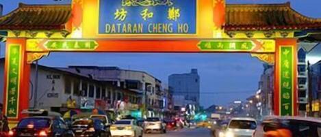 Escena callejera con un arco tradicional chino que dice "DATARAN CHENG HO" al anochecer.
