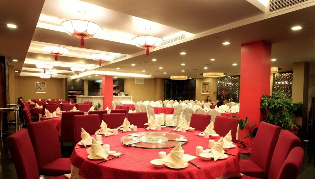Une salle de banquet avec des tables rondes recouvertes de nappes rouges et de serviettes blanches, des chaises rouges et des éléments de décoration rouge.