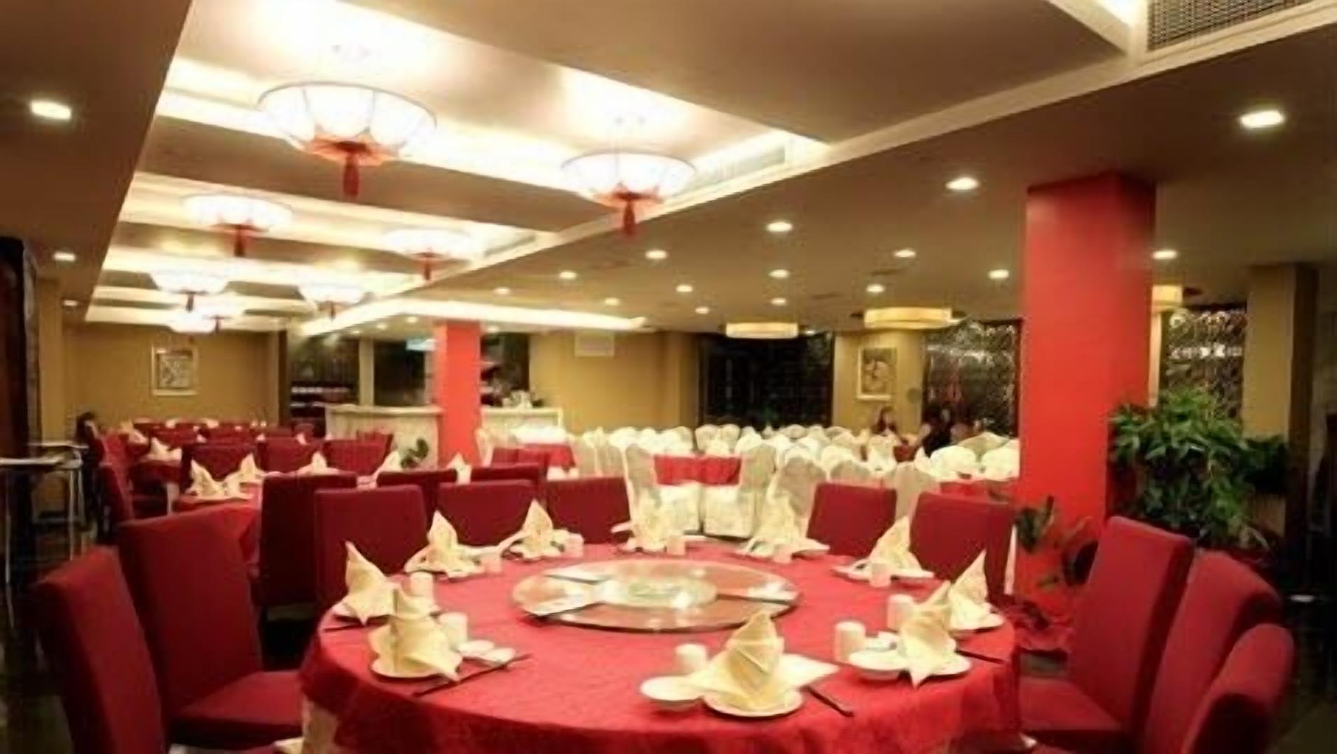 Een feestzaal met ronde tafels, bedekt met rode tafelkleden, witte servetten en borden.