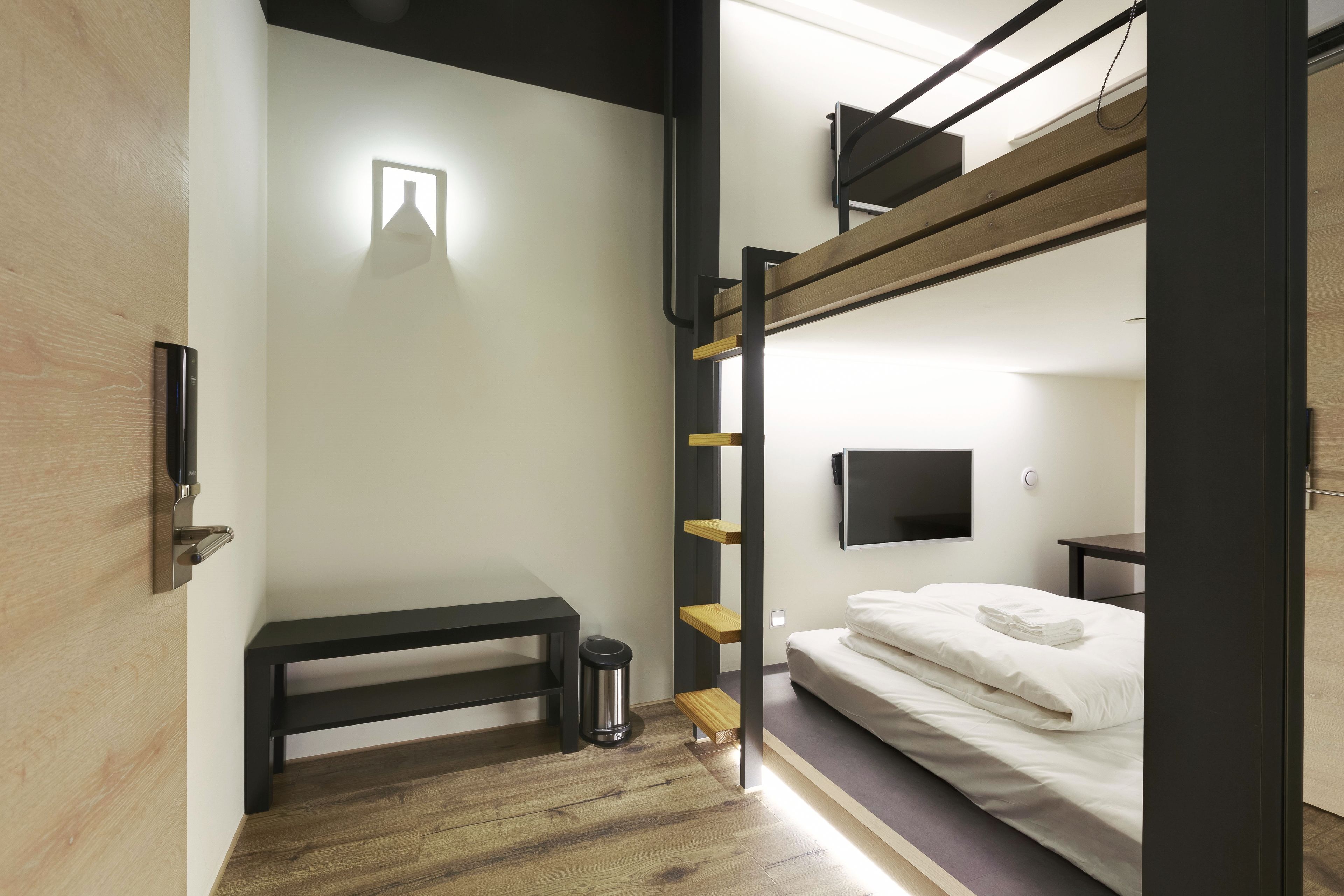 A bunk bed room with a desk, a trash can, and a TV mounted on the wall.