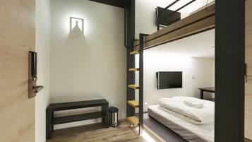 A bunk bed room with a desk, a trash can, and a TV mounted on the wall.