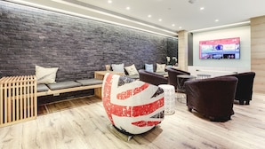 A modern lounge area with a brick wall, wooden seating, a unique red and white spherical chair, and a flat-screen TV on the wall. - Taiwan Youth Hostel & Capsule Hostel (Taipei)