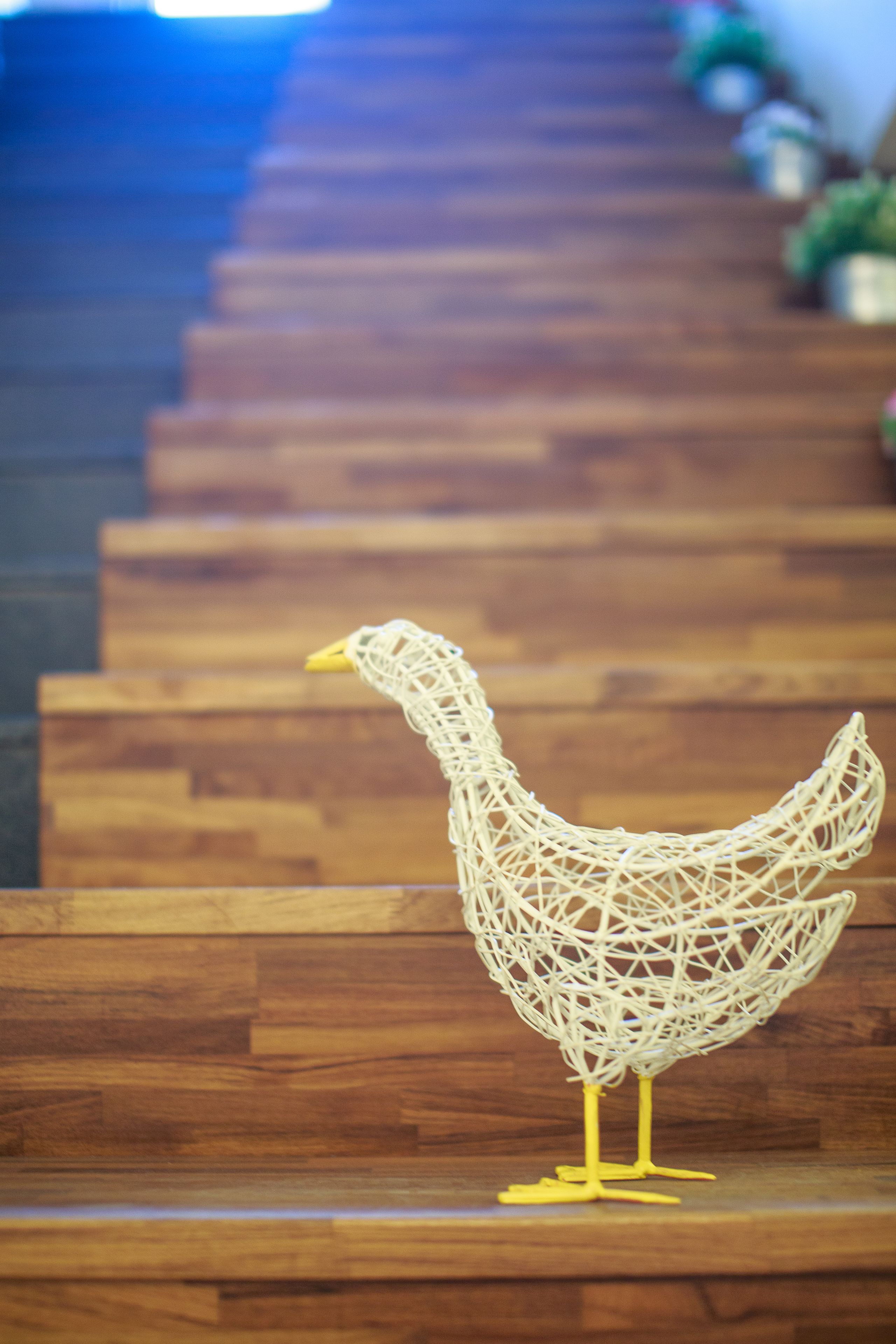 A white, intricately woven sculpture of a chicken on wooden steps.