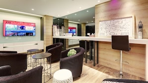 A modern lounge area with comfortable seating, a bar counter, and a large flat-screen TV displaying news. - Taiwan Youth Hostel & Capsule Hostel (Taipei)