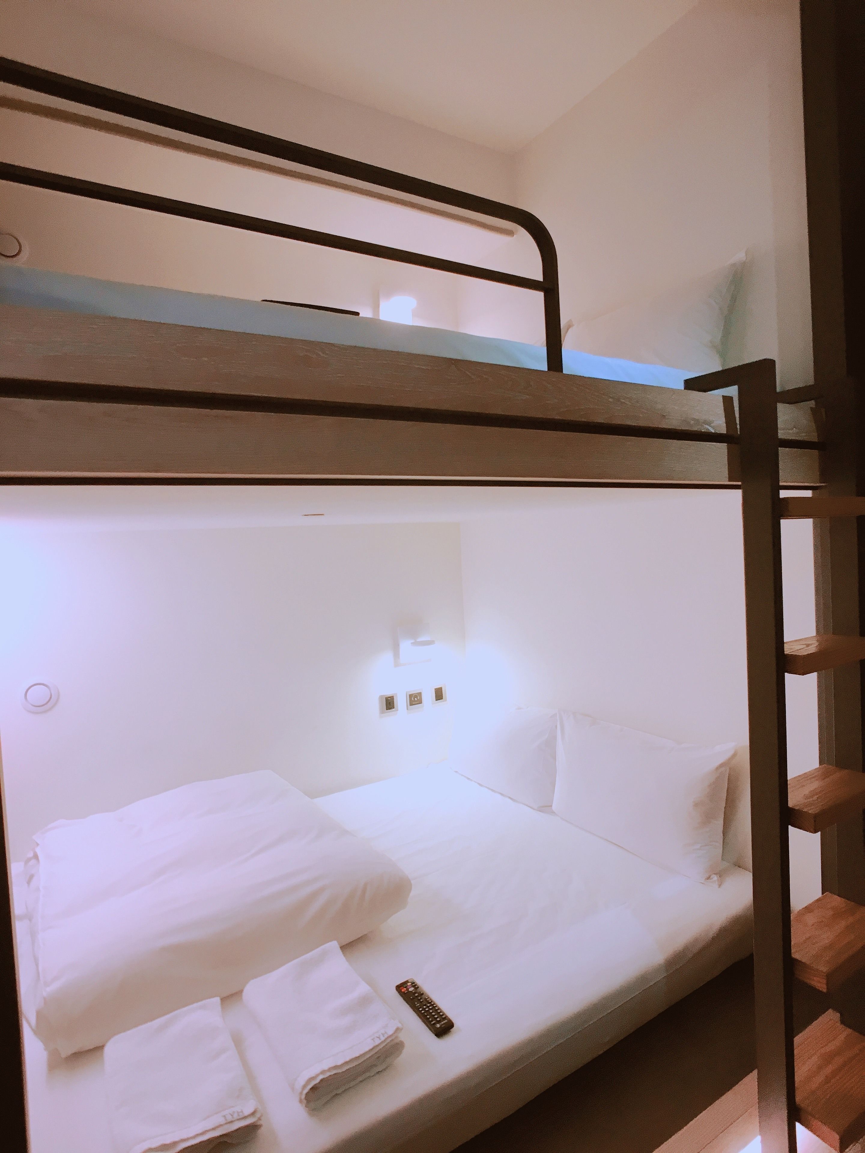 Una cama litera con ropa de cama blanca y un control remoto en la cama inferior.