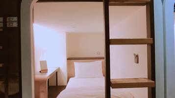 A bunk bed with a ladder, a bedside table, and a nightstand in a room with a white wall and a window.