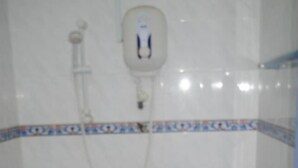 Un baño pequeño con un inodoro azul, una pared blanca con un borde de azulejos azules y blancos, y un calentador de agua blanco instalado en la pared.